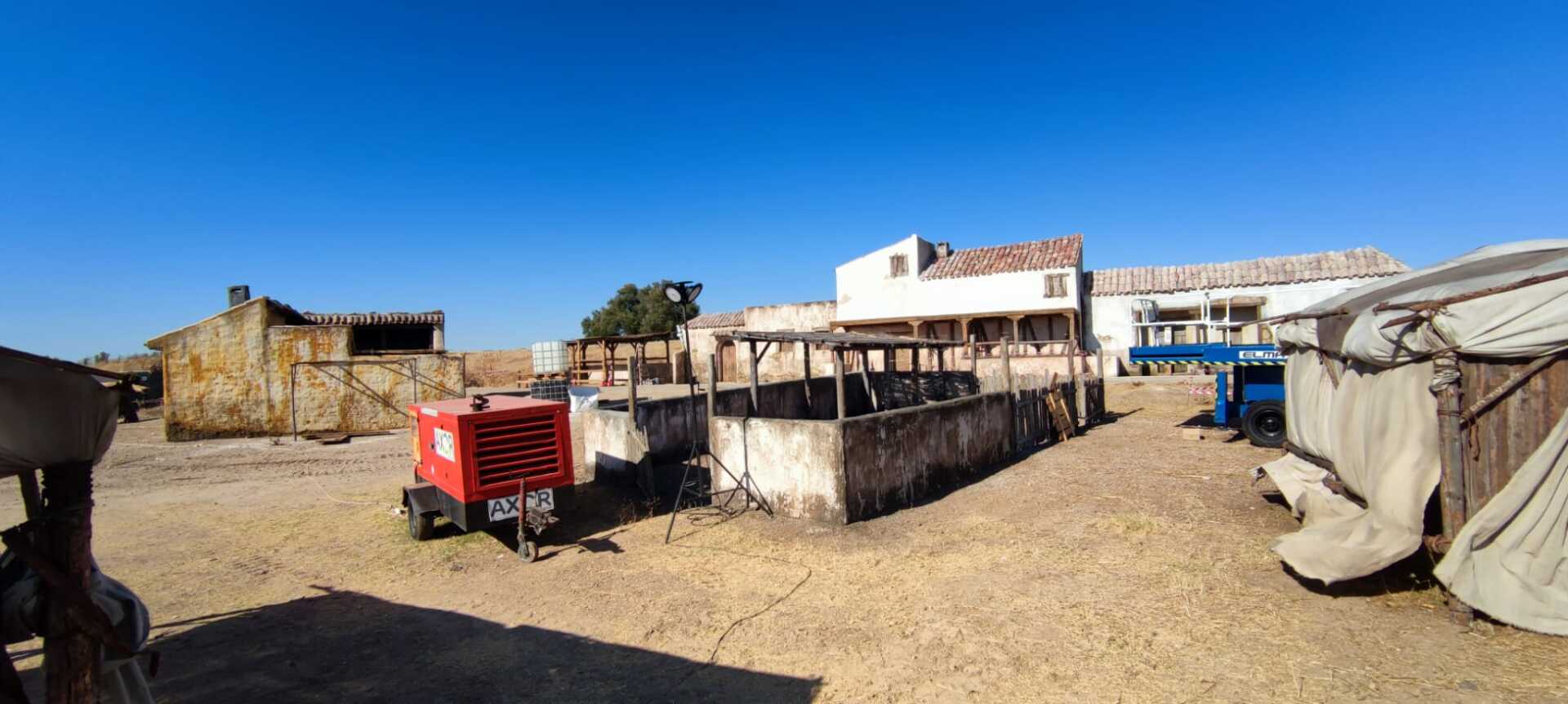 Un tractor rojo está estacionado en un campo de tierra frente a un edificio.
