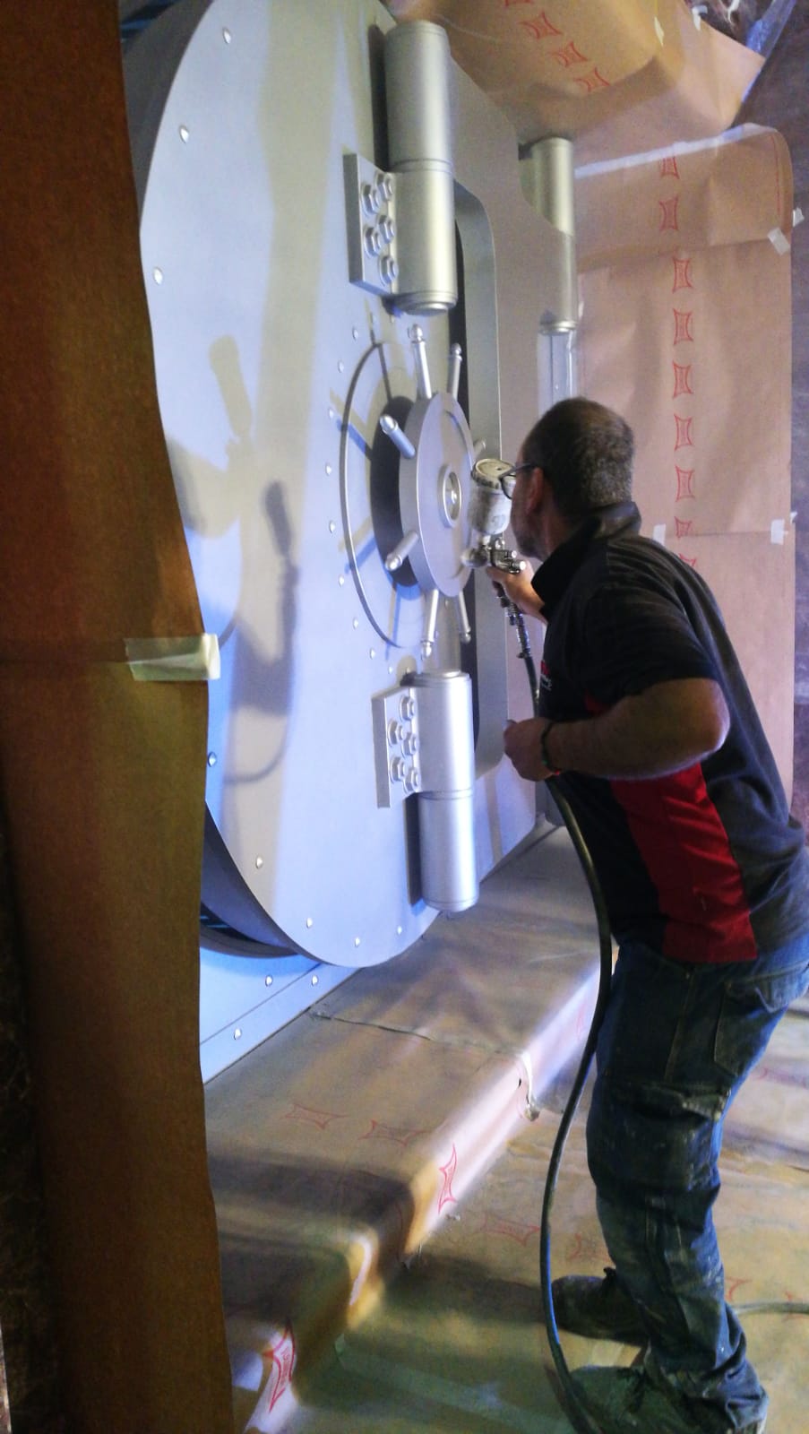 Un hombre está pintando con aerosol la puerta de una bóveda en una habitación.