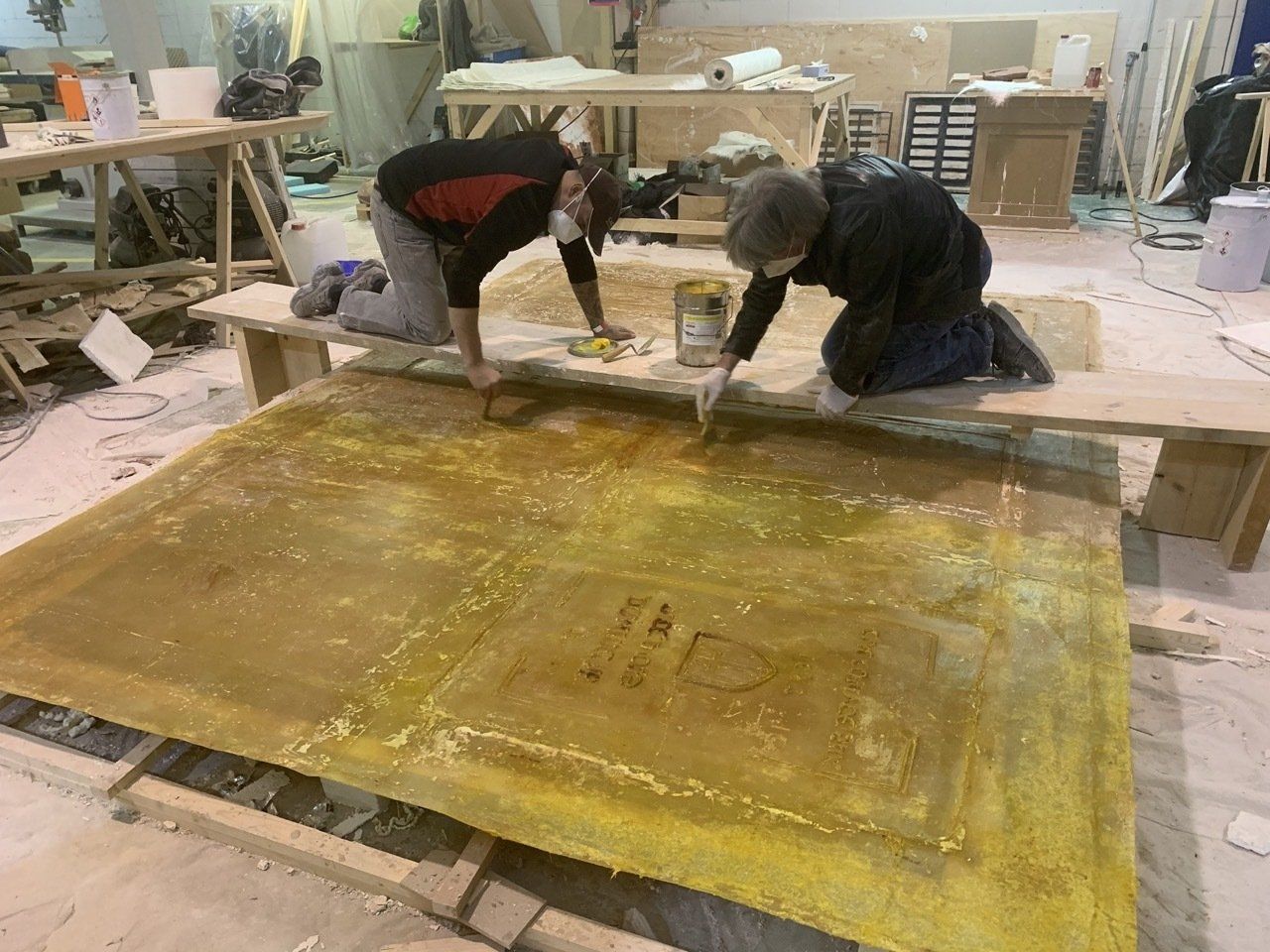 Dos personas están trabajando en un gran trozo de madera en un taller.