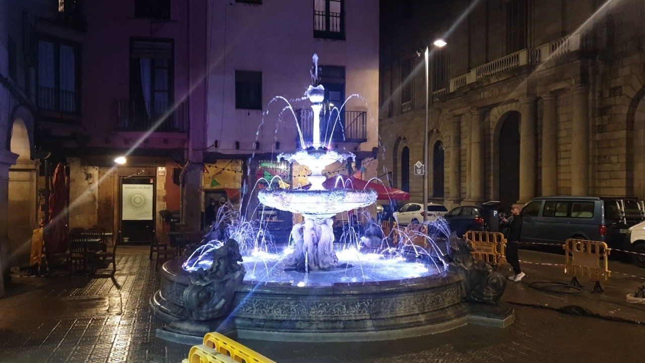 Una fuente se ilumina por la noche frente a un edificio.