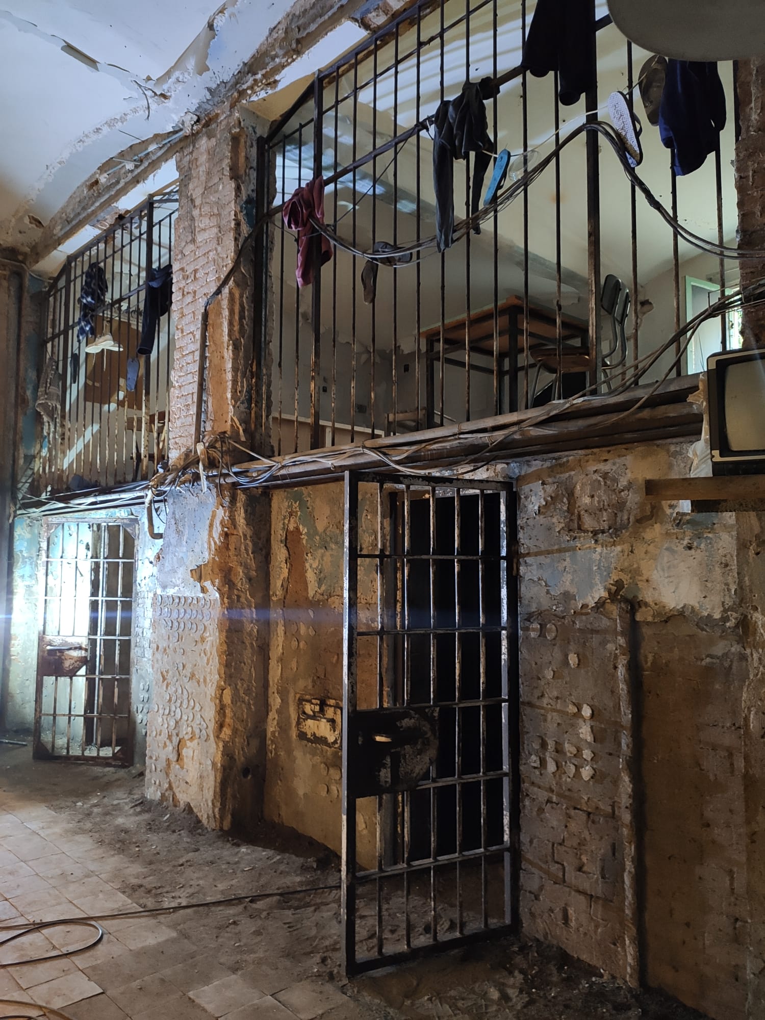 Una celda de prisión con ropa colgada en los barrotes y una puerta.