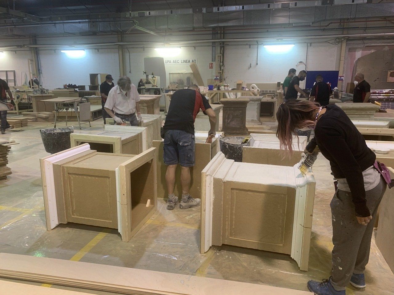 Un grupo de personas está trabajando en gabinetes de madera en una fábrica.