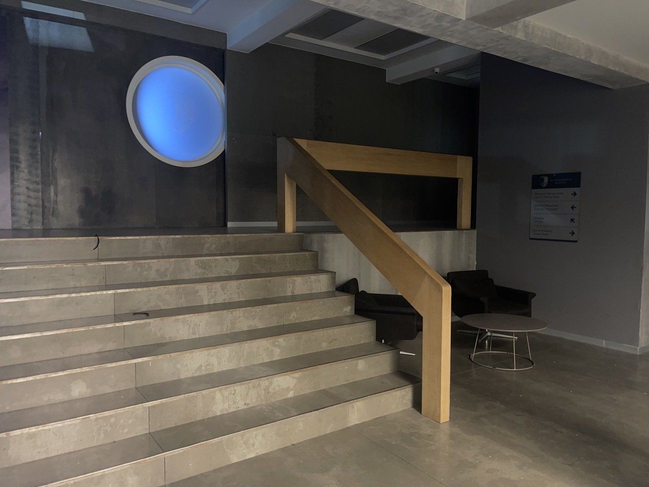 Una escalera con barandilla de madera y una luz azul en la pared.