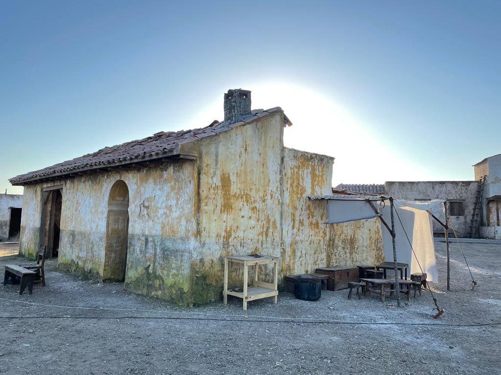 Un edificio viejo con techo y chimenea en medio de un campo de tierra.