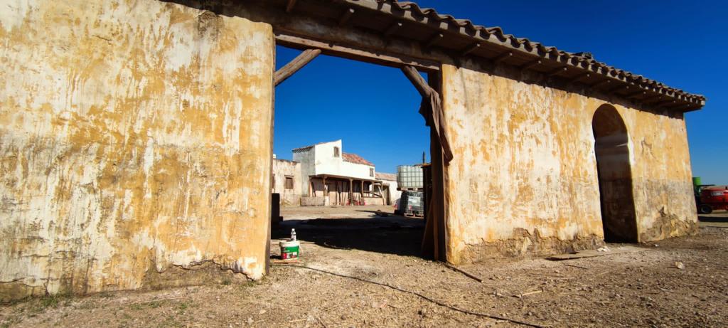 Un edificio antiguo con un arco de madera que conduce a un camino de tierra.