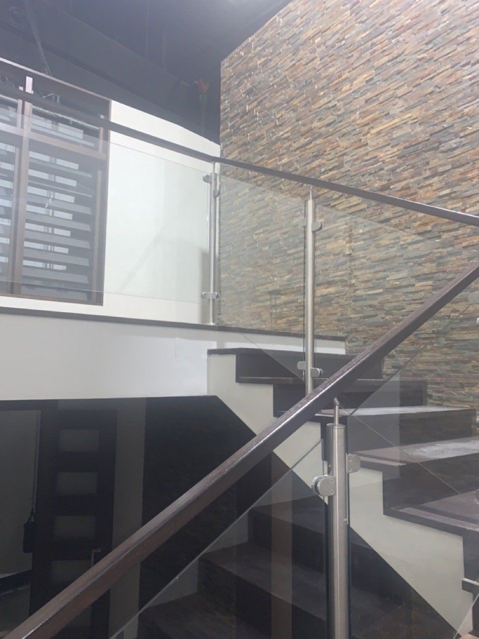 Una escalera con barandilla de cristal y una pared de piedra.