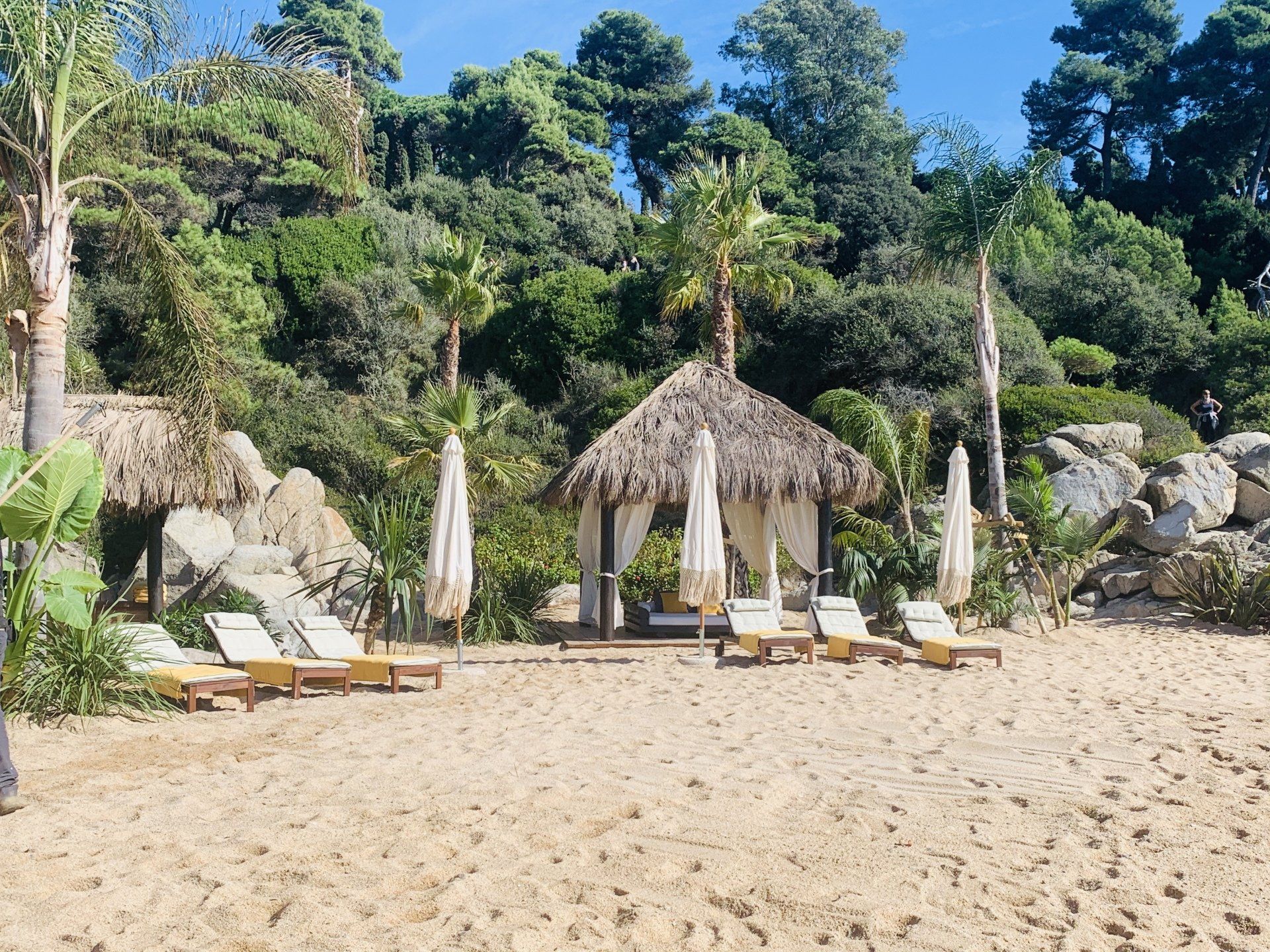Una playa con sillas y sombrillas y una cabaña al fondo.