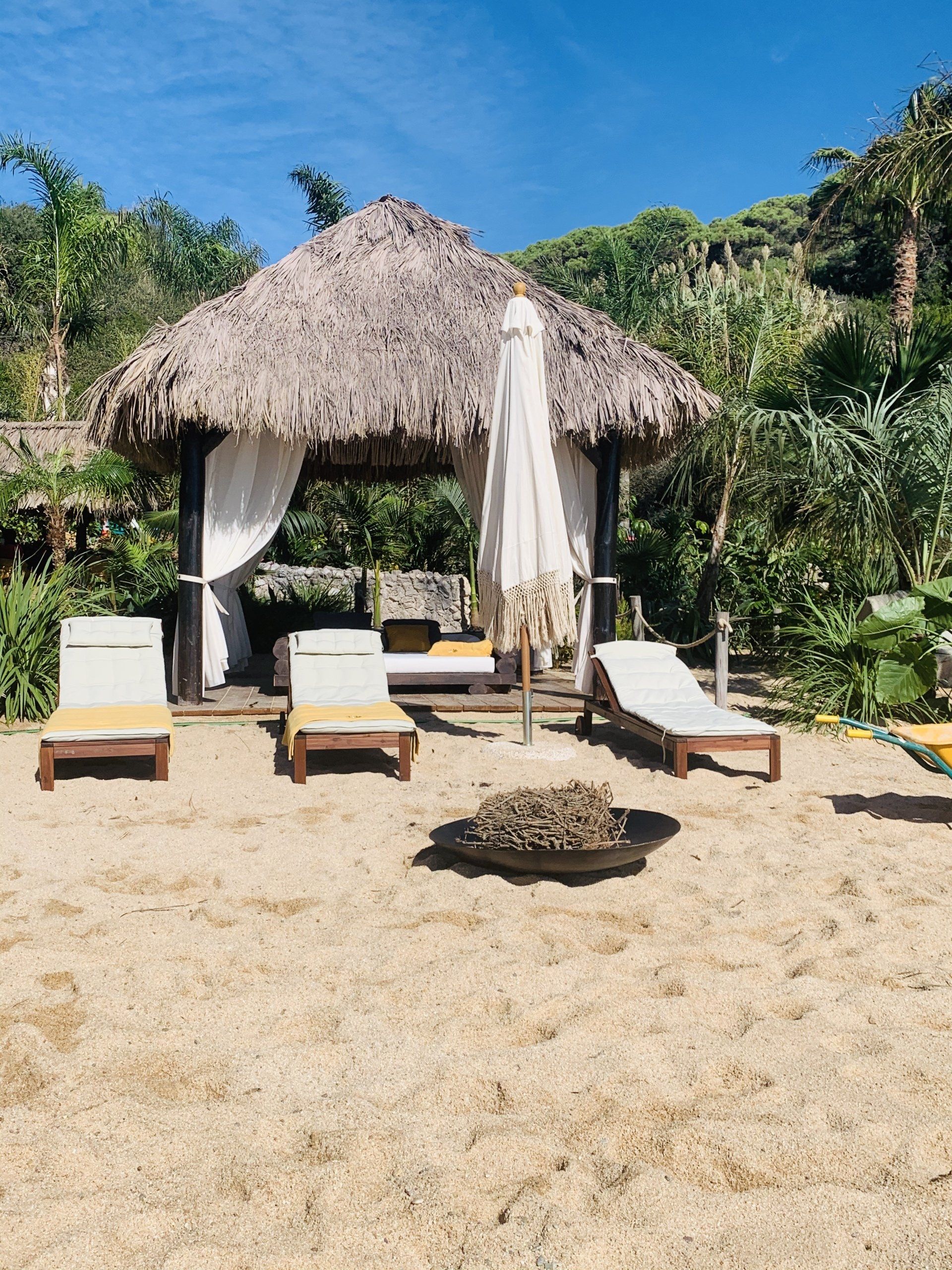 Una choza de paja en una playa con sillas y sombrillas