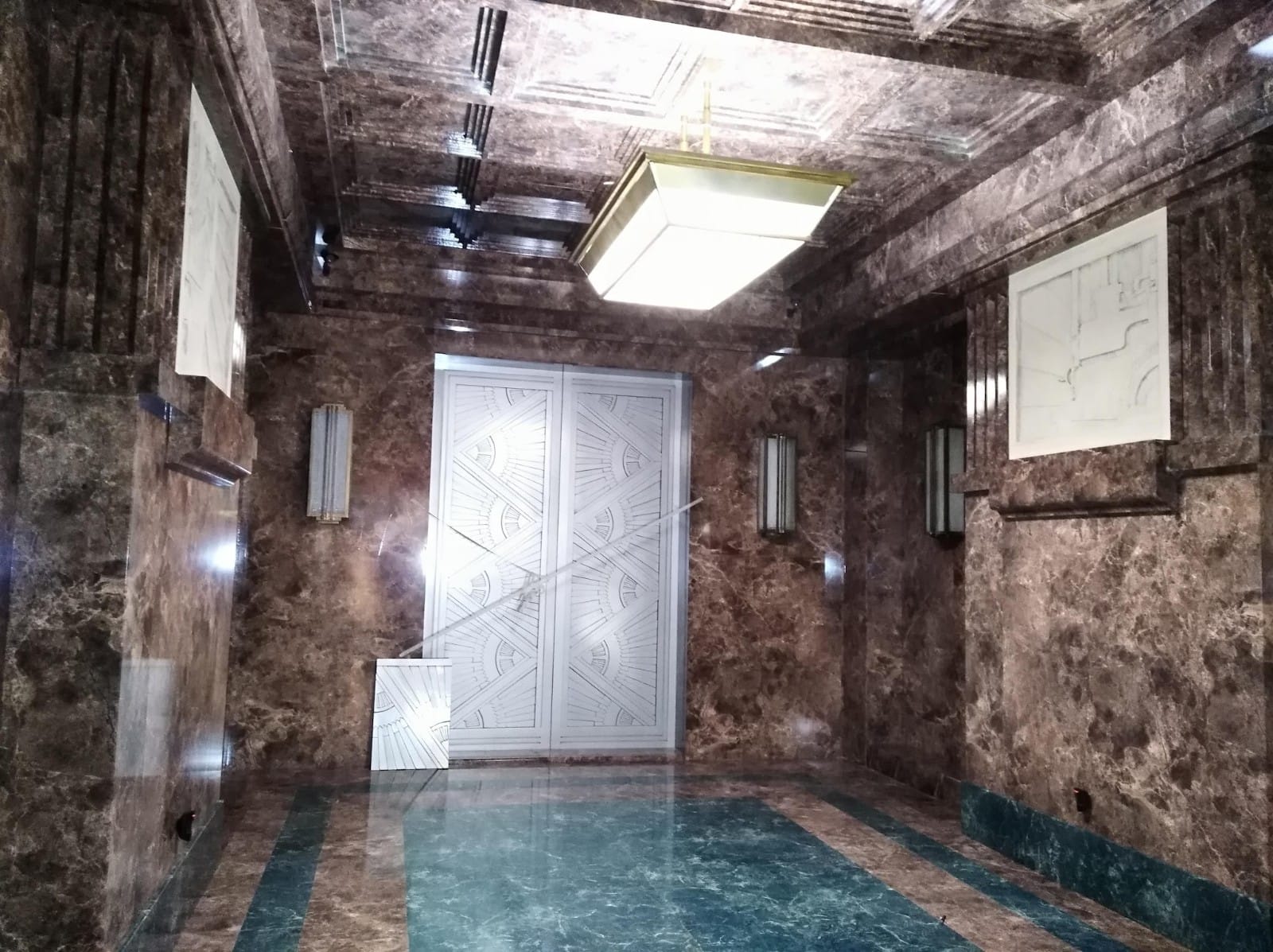 Un pasillo con paredes de mármol y una lámpara de techo.