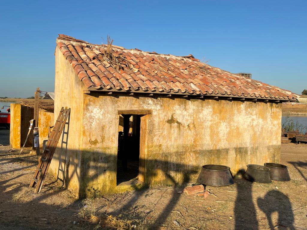 Un viejo edificio con techo de tejas se encuentra en medio de un campo de tierra.