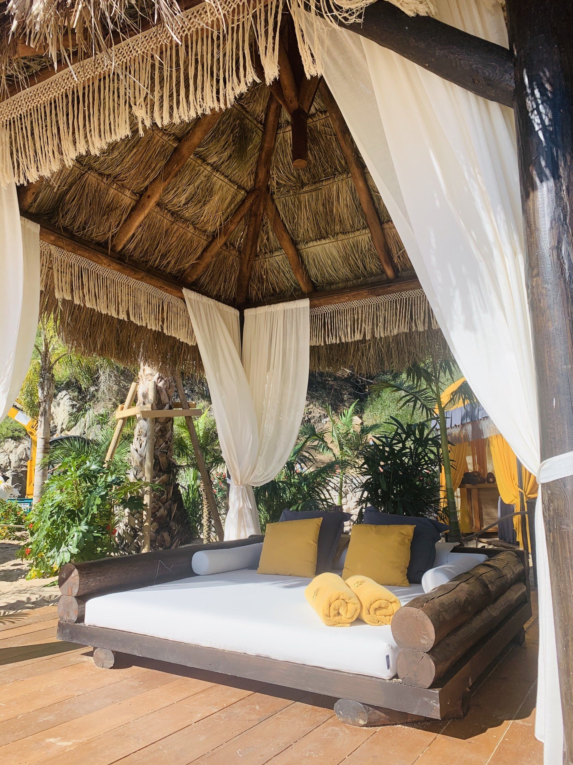 Un cenador con techo de paja y una cama debajo.