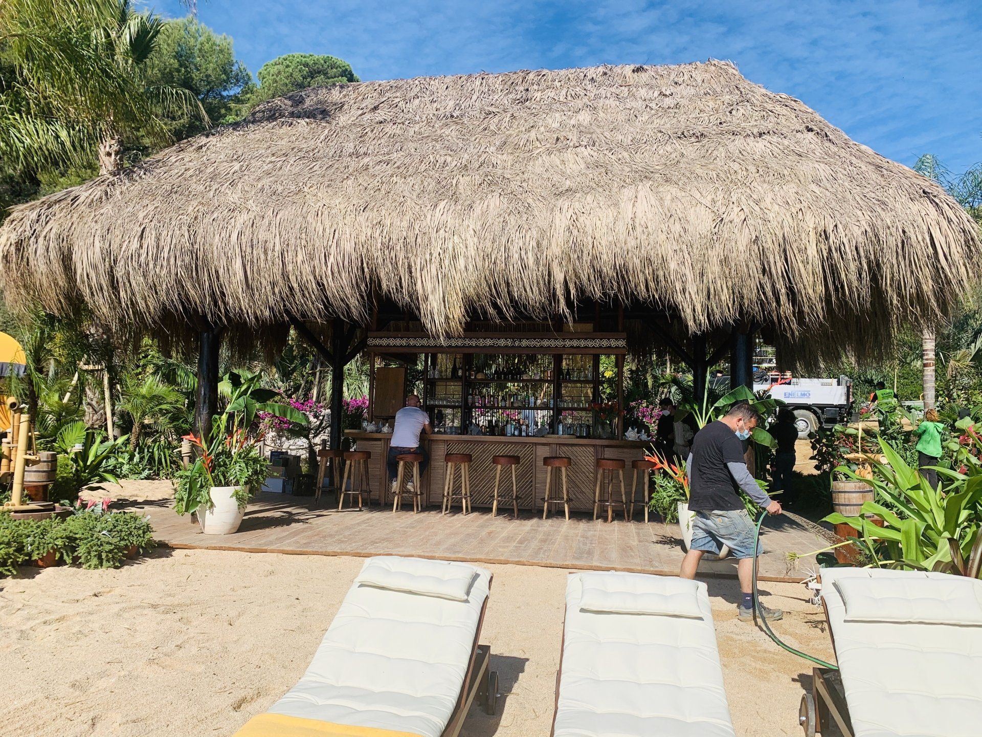 Un hombre está parado frente a una choza con techo de paja en una playa.