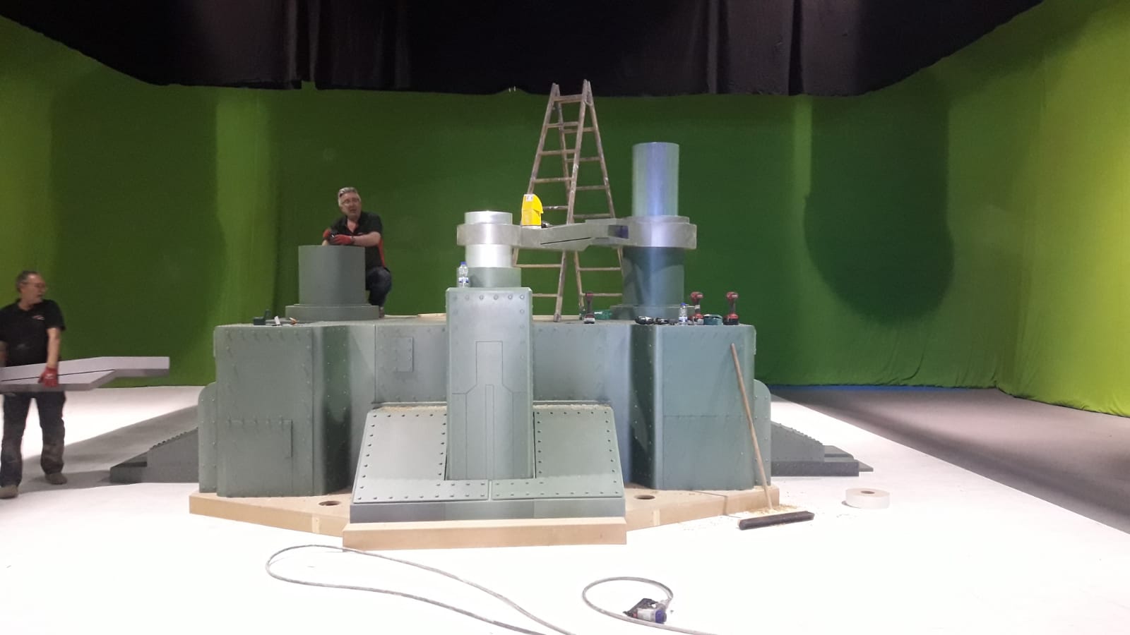 Dos hombres están parados frente a una pantalla verde en una habitación.