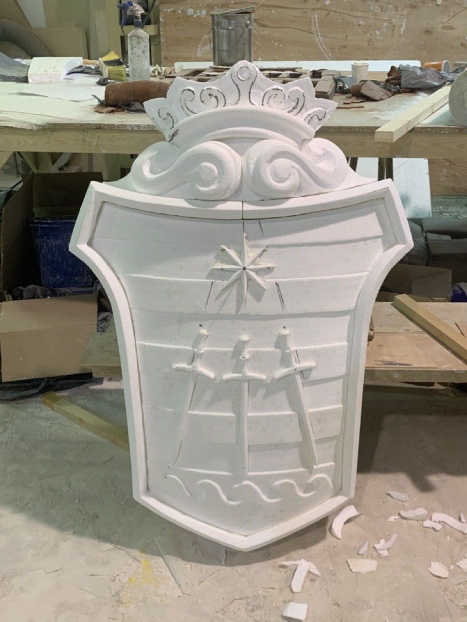 Un escudo blanco con una corona en la parte superior está sobre una mesa.