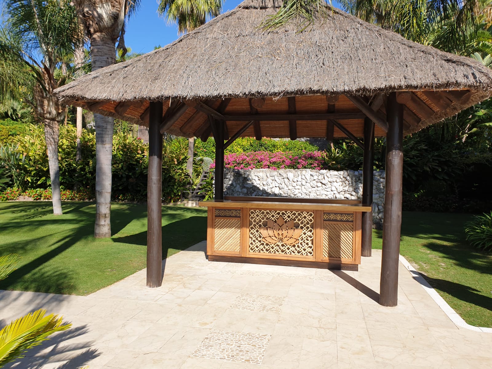 Un cenador con techo de paja y una mesa de madera debajo.