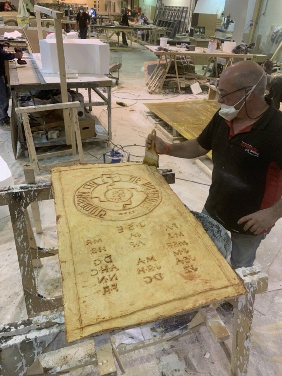 Un hombre que lleva una máscara está pintando un trozo de madera.