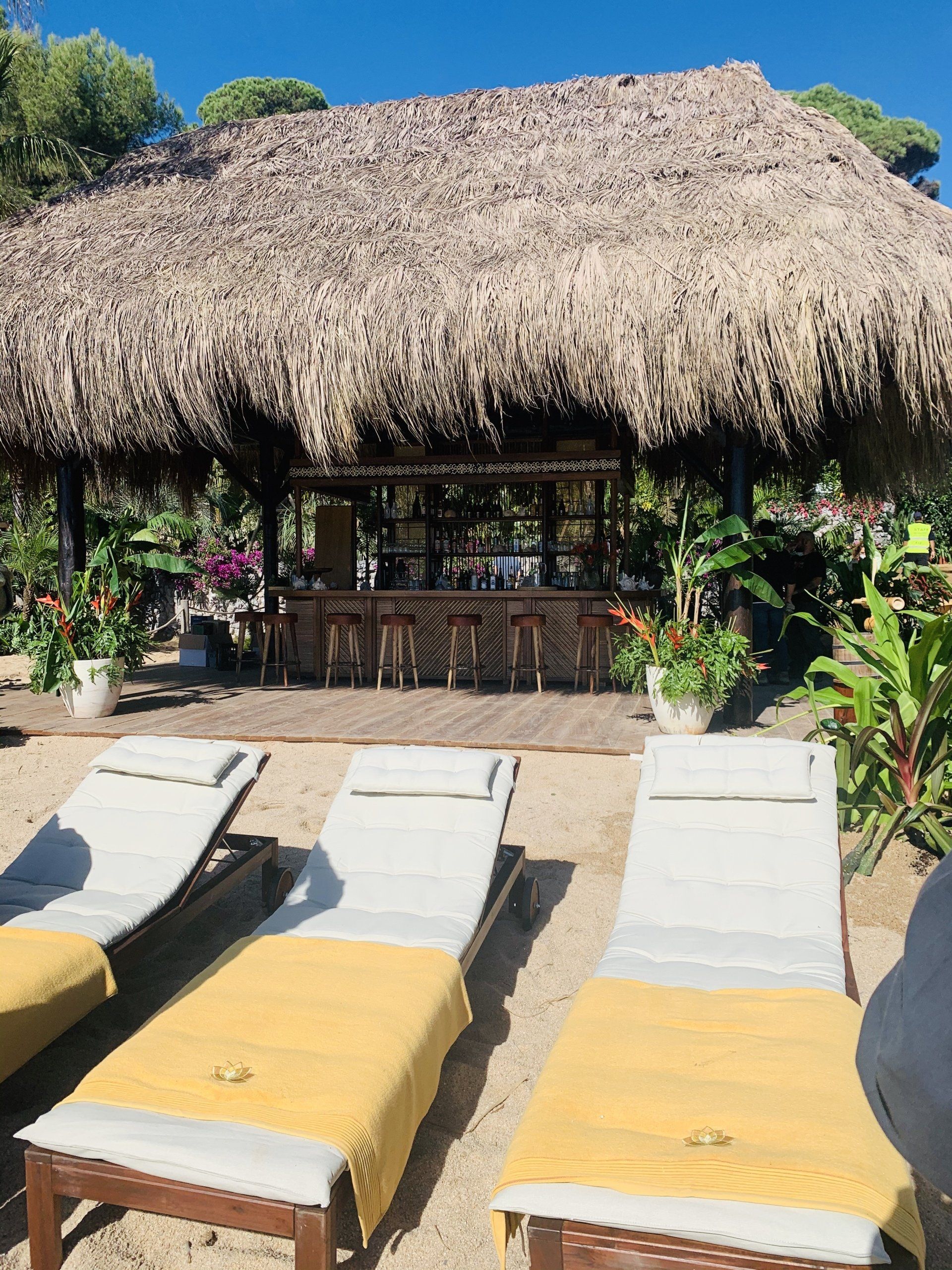 Una cabaña con techo de paja con bar y tumbonas en la playa.