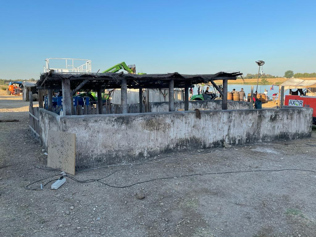 Una gran estructura de hormigón con techo de madera se encuentra en medio de un campo de tierra.