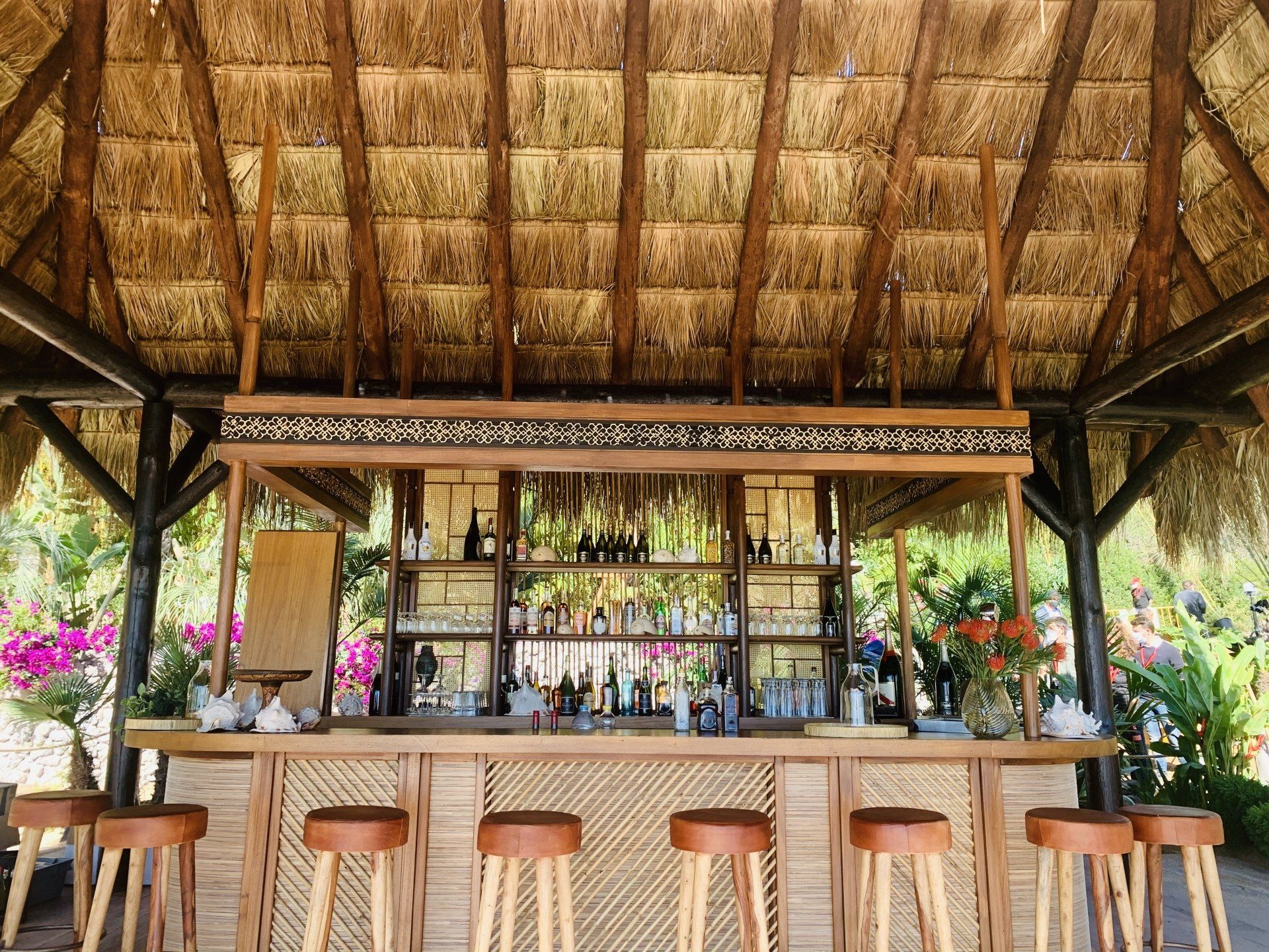 Un bar de madera con taburetes bajo un techo de paja.