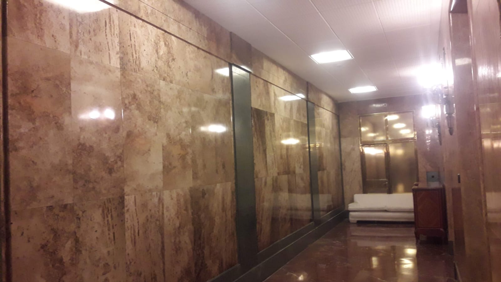 Un largo pasillo con paredes de mármol y un sofá blanco.