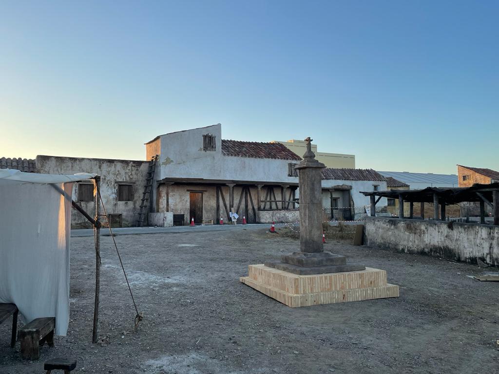 Hay una estatua en el medio de un campo de tierra frente a un edificio.