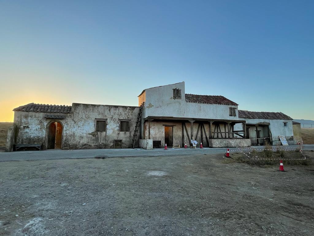 Un gran edificio blanco con techo rojo está situado en medio de un campo de tierra.