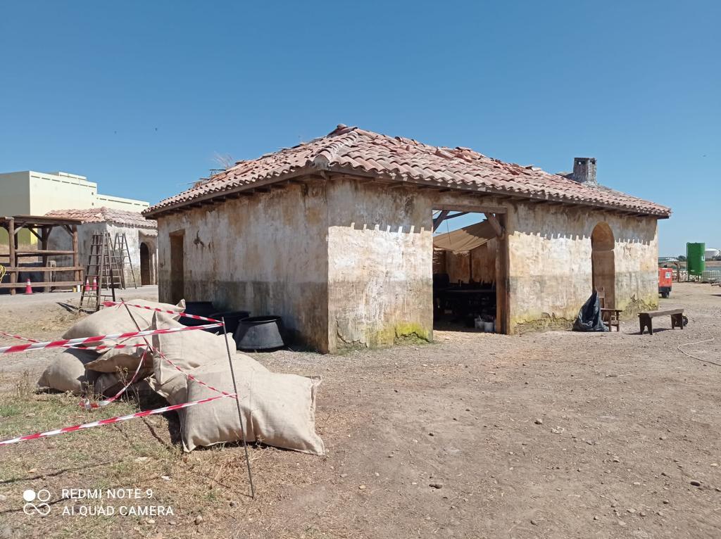 Un pequeño edificio con techo de tejas se encuentra en medio de un campo de tierra.