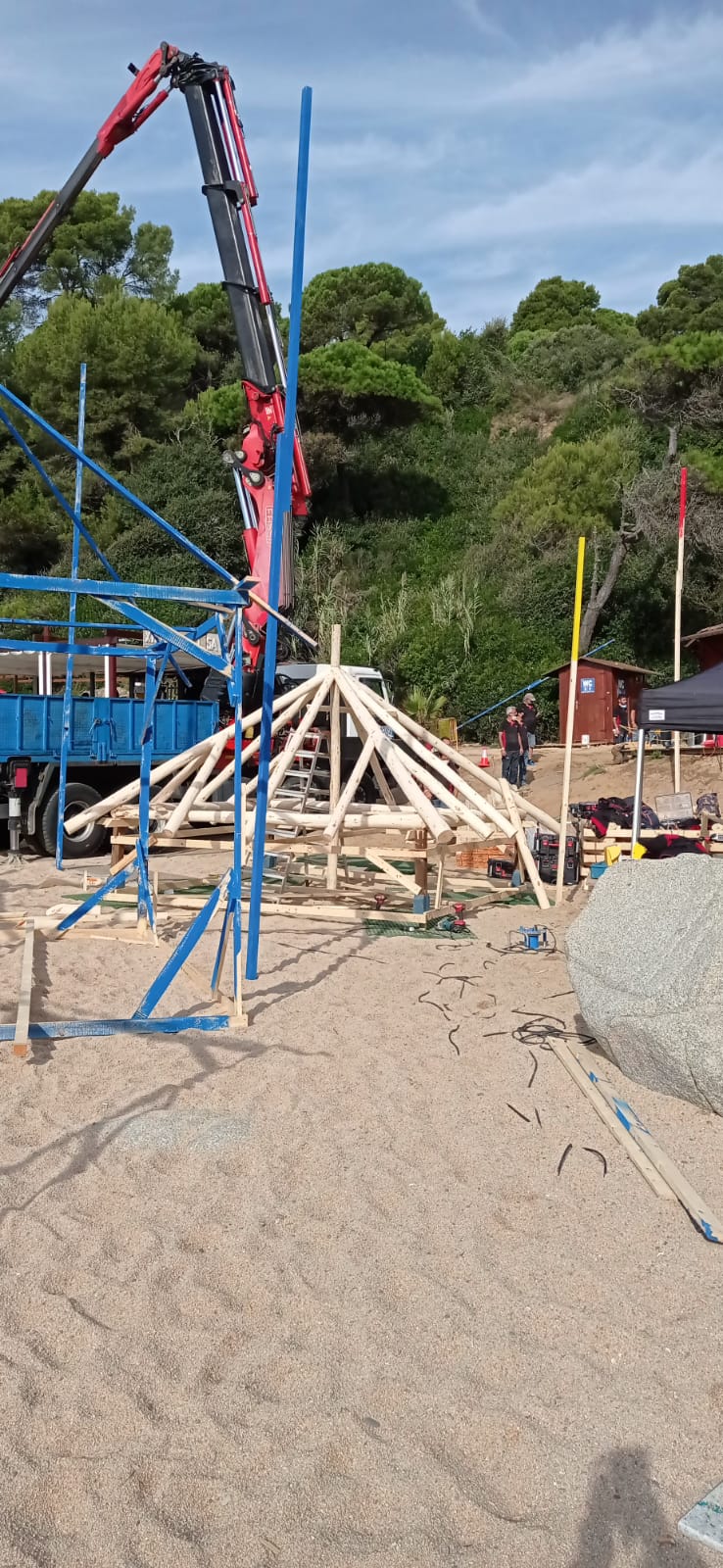 Una grúa está levantando una estructura de madera en una playa.