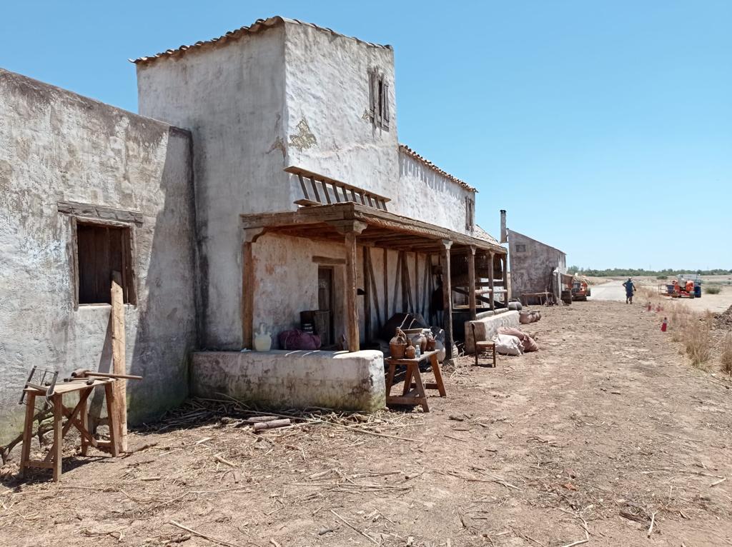 Un edificio blanco con un porche en medio de un campo de tierra.