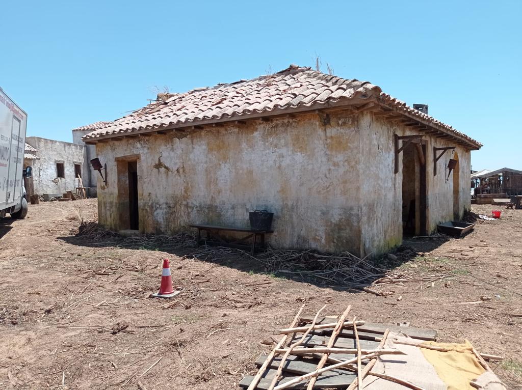 Un viejo edificio con techo de tejas se encuentra en medio de un campo de tierra.