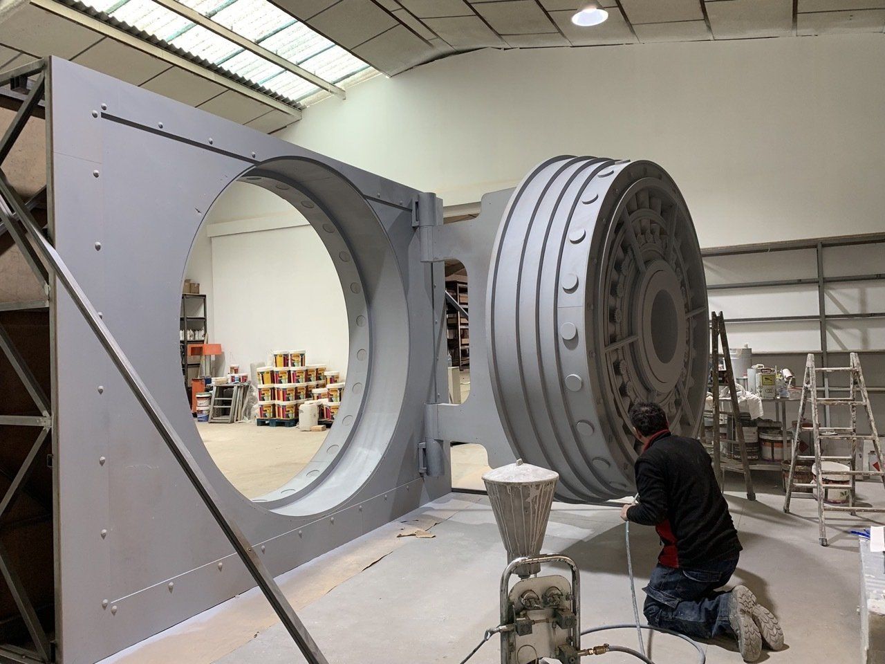 Un hombre está arrodillado frente a una gran puerta bóveda en un almacén.