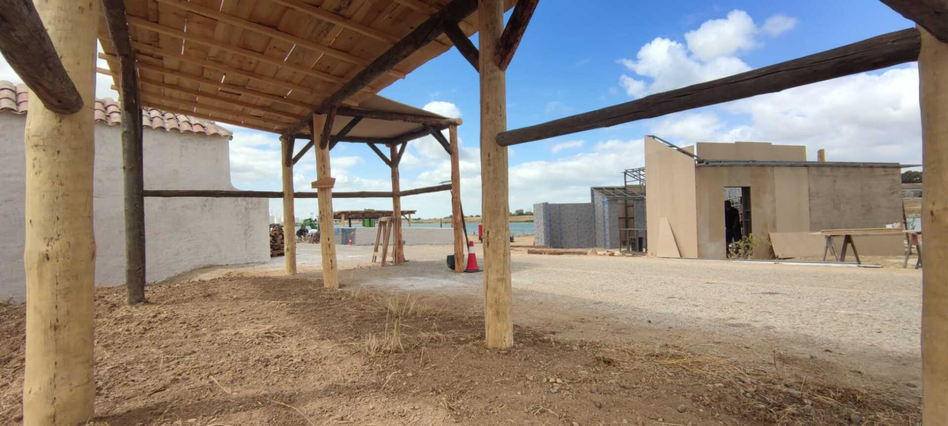 Una estructura de madera con techo de paja está en medio de un campo de tierra.