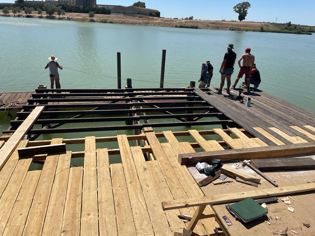 Un grupo de personas de pie en un muelle de madera con vistas a un cuerpo de agua.