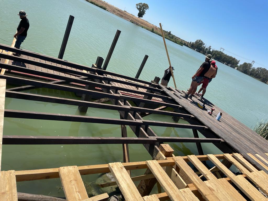 Un grupo de personas está trabajando en un muelle de madera con vista a un cuerpo de agua.