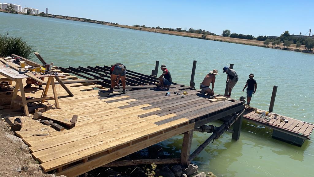 Un grupo de personas está trabajando en un muelle de madera al lado de un cuerpo de agua.