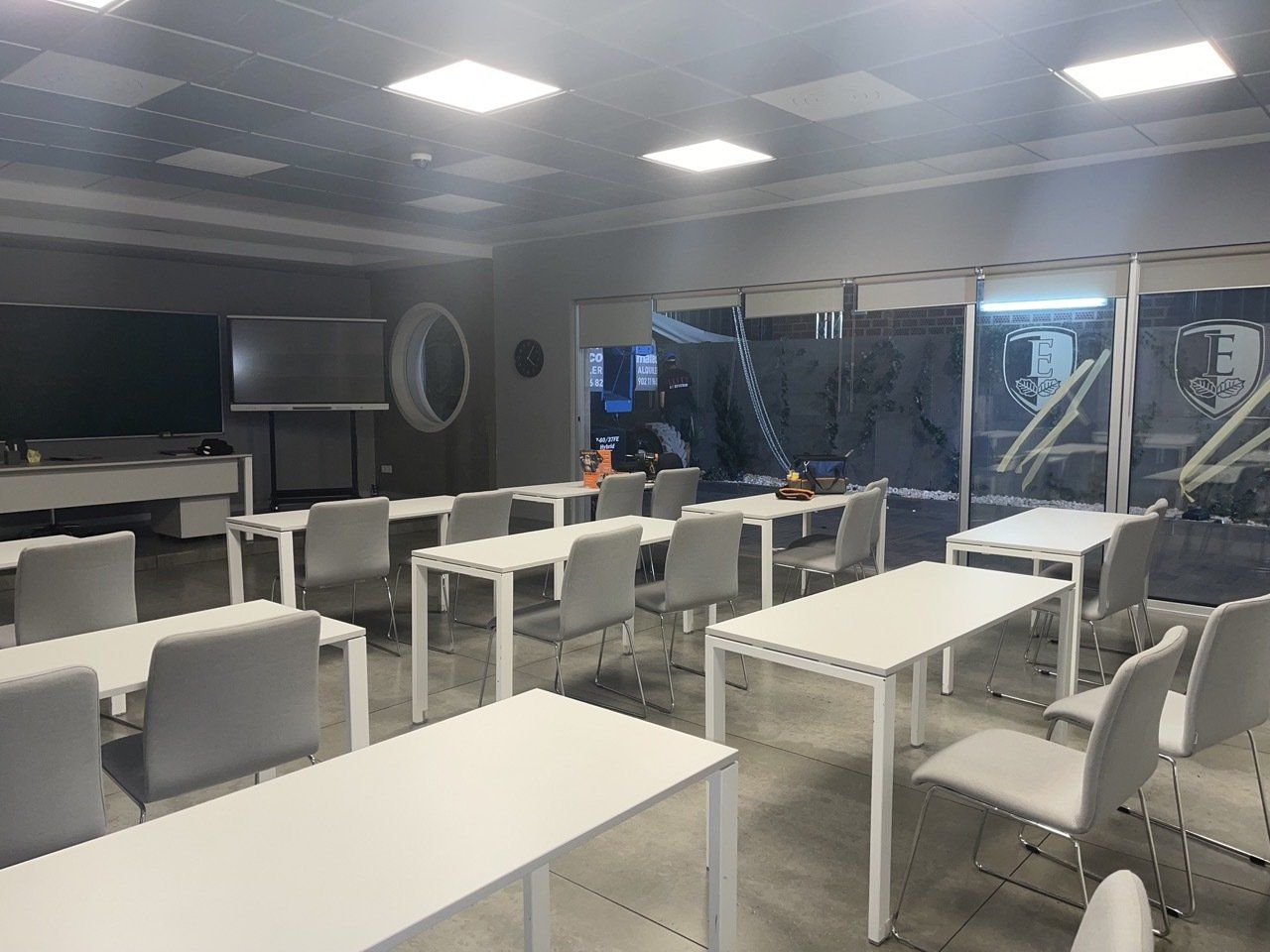 Un aula con mesas y sillas blancas y una ventana grande.