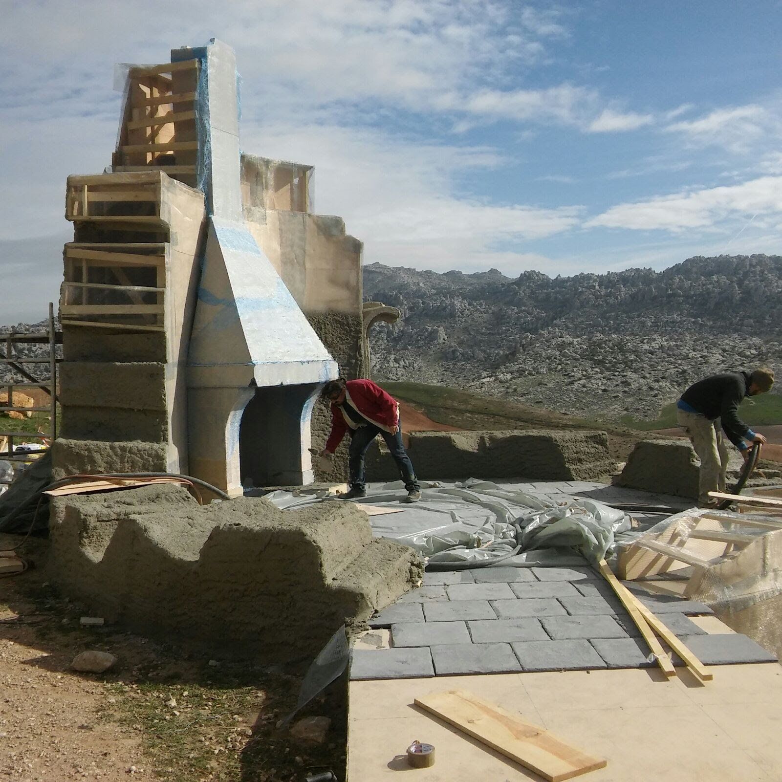 Dos hombres están trabajando en un sitio de construcción con montañas al fondo.