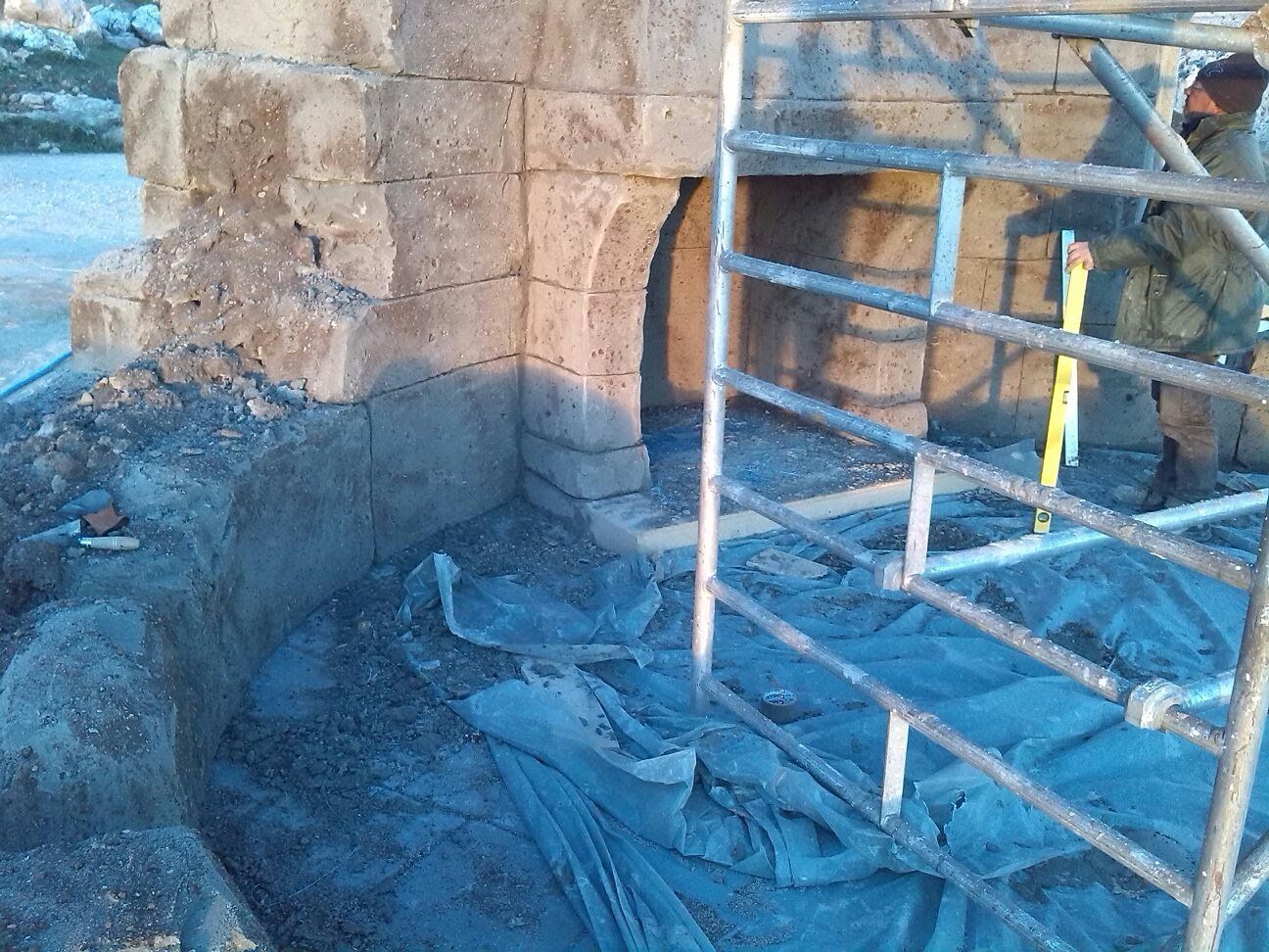 Un hombre está de pie sobre un andamio junto a un muro de piedra.