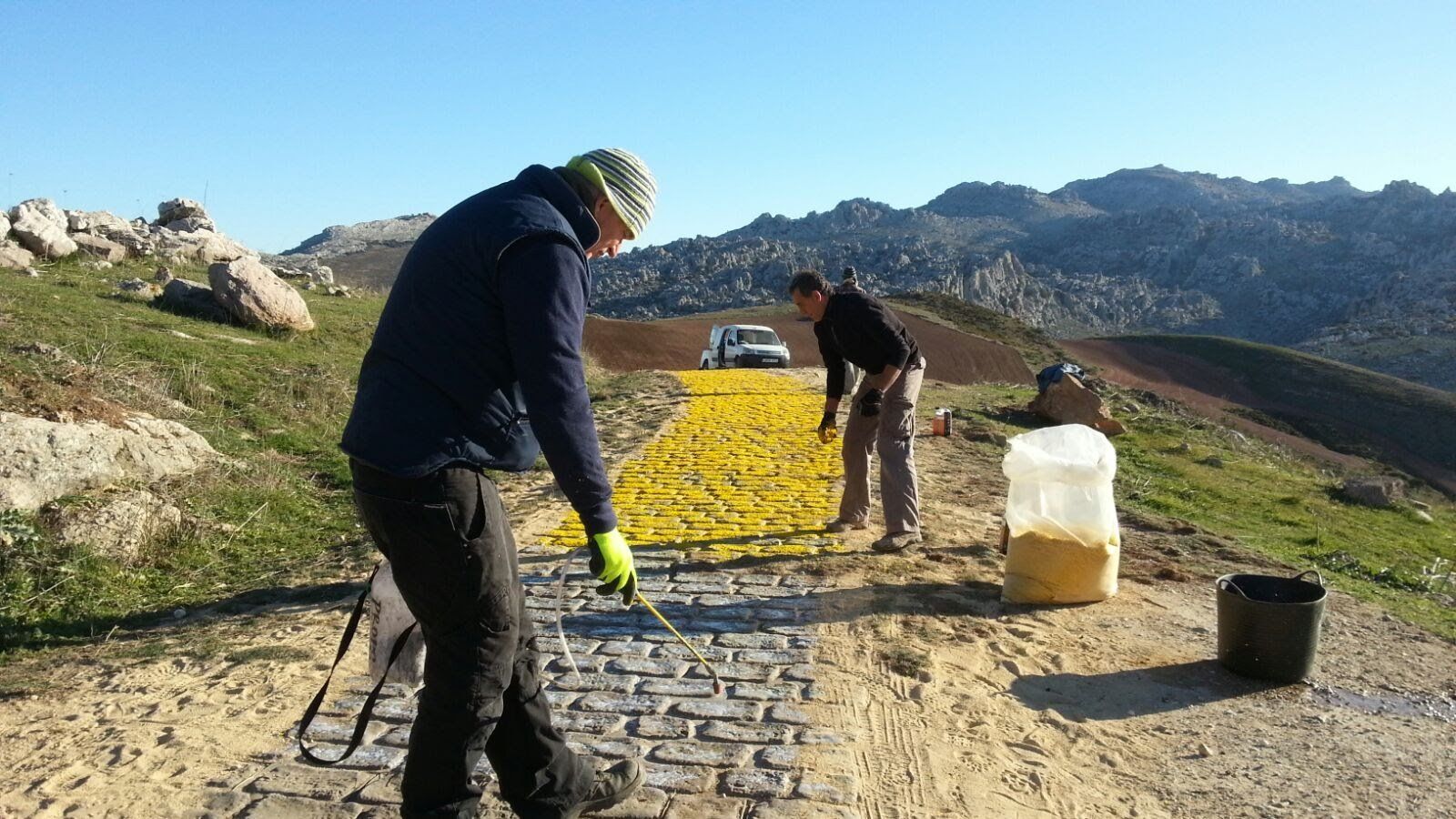 Dos hombres están pintando una carretera con pintura amarilla.