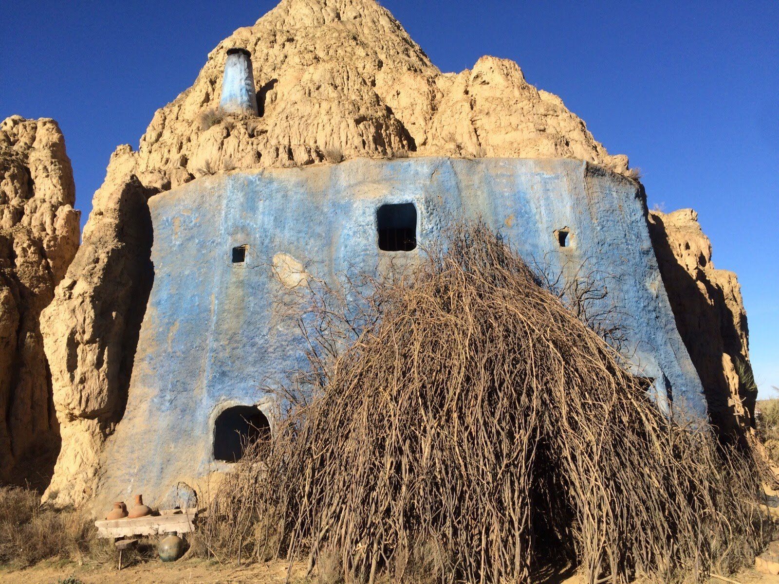 Un edificio azul con techo de paja en el desierto.