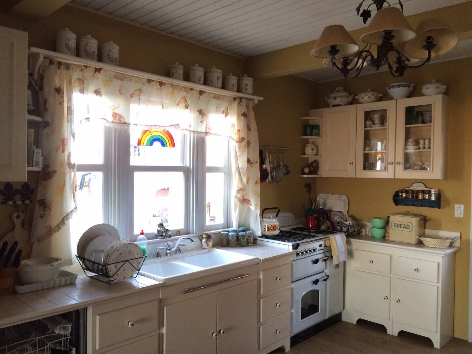 Una cocina con fregadero, estufa, lavavajillas y una ventana con un arcoíris en ella.