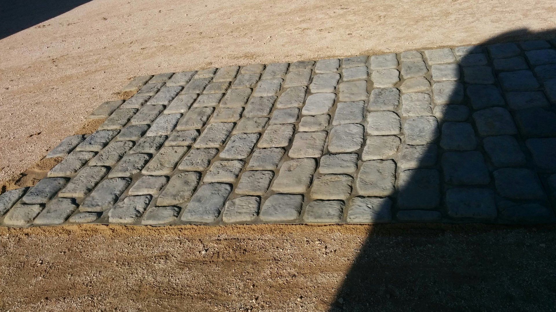 La sombra de una persona se proyecta sobre un camino adoquinado.