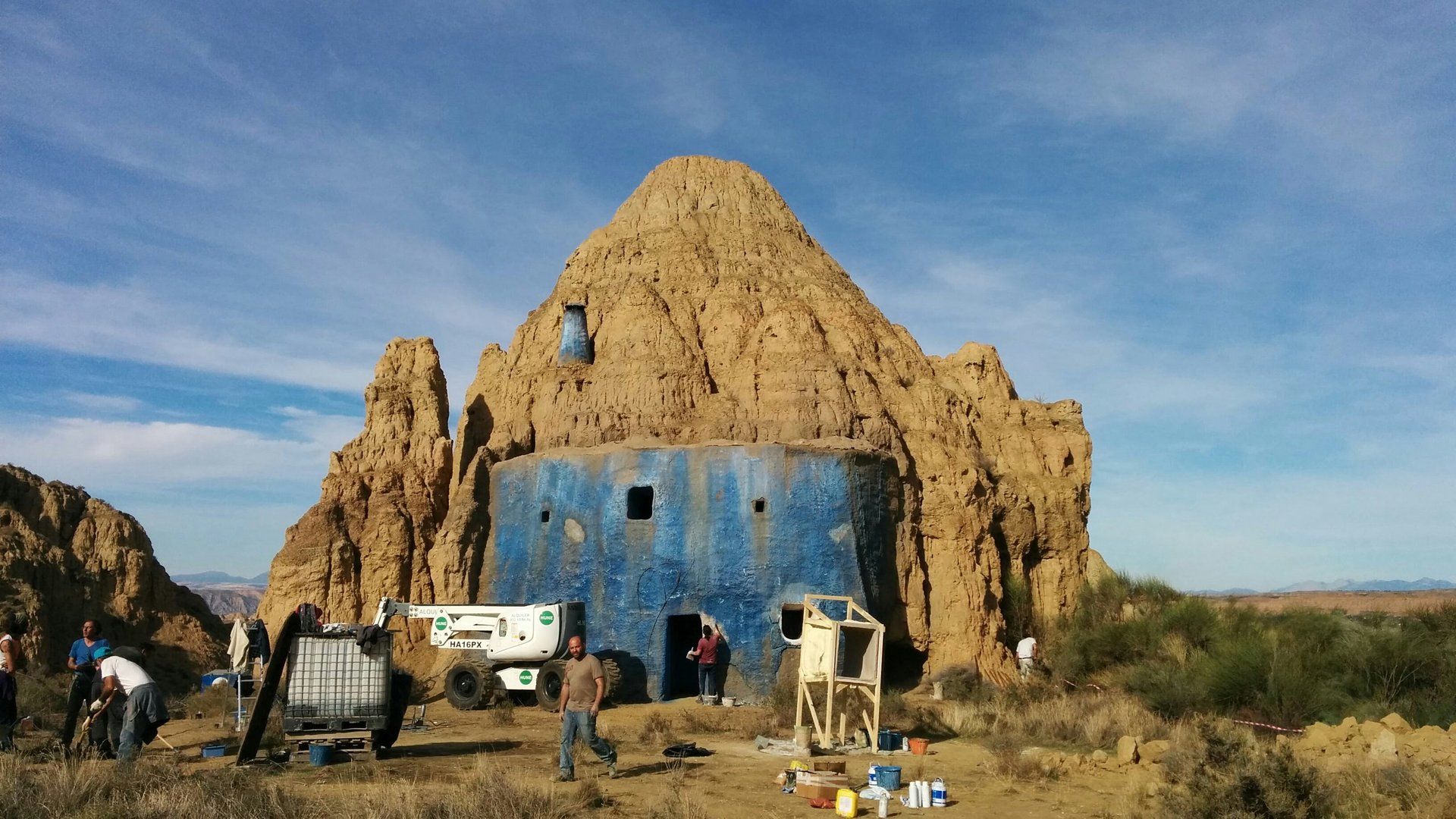 Un grupo de personas está parado frente a un edificio azul en medio de un desierto.
