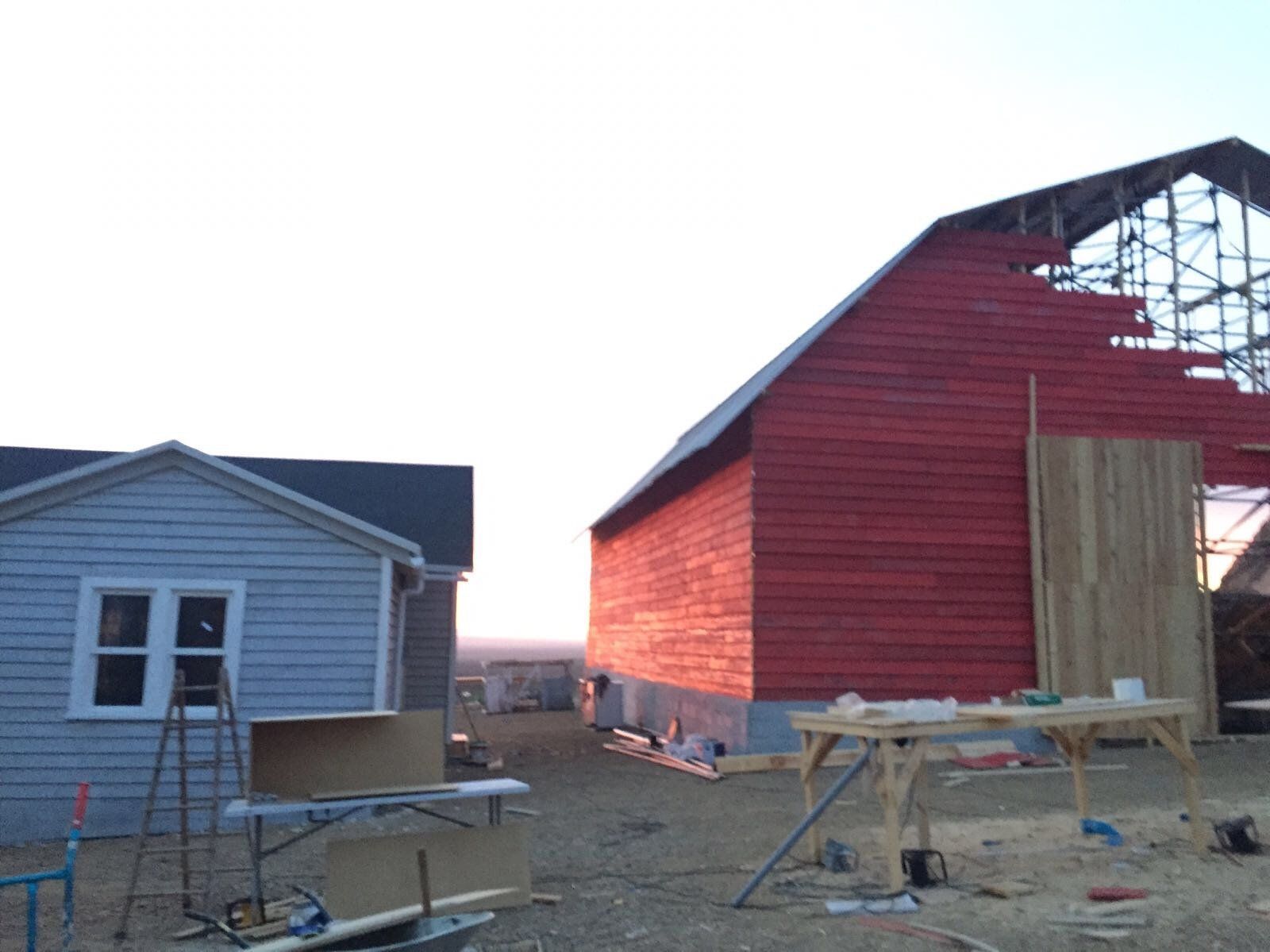 Se está construyendo un granero rojo al lado de una casa gris.