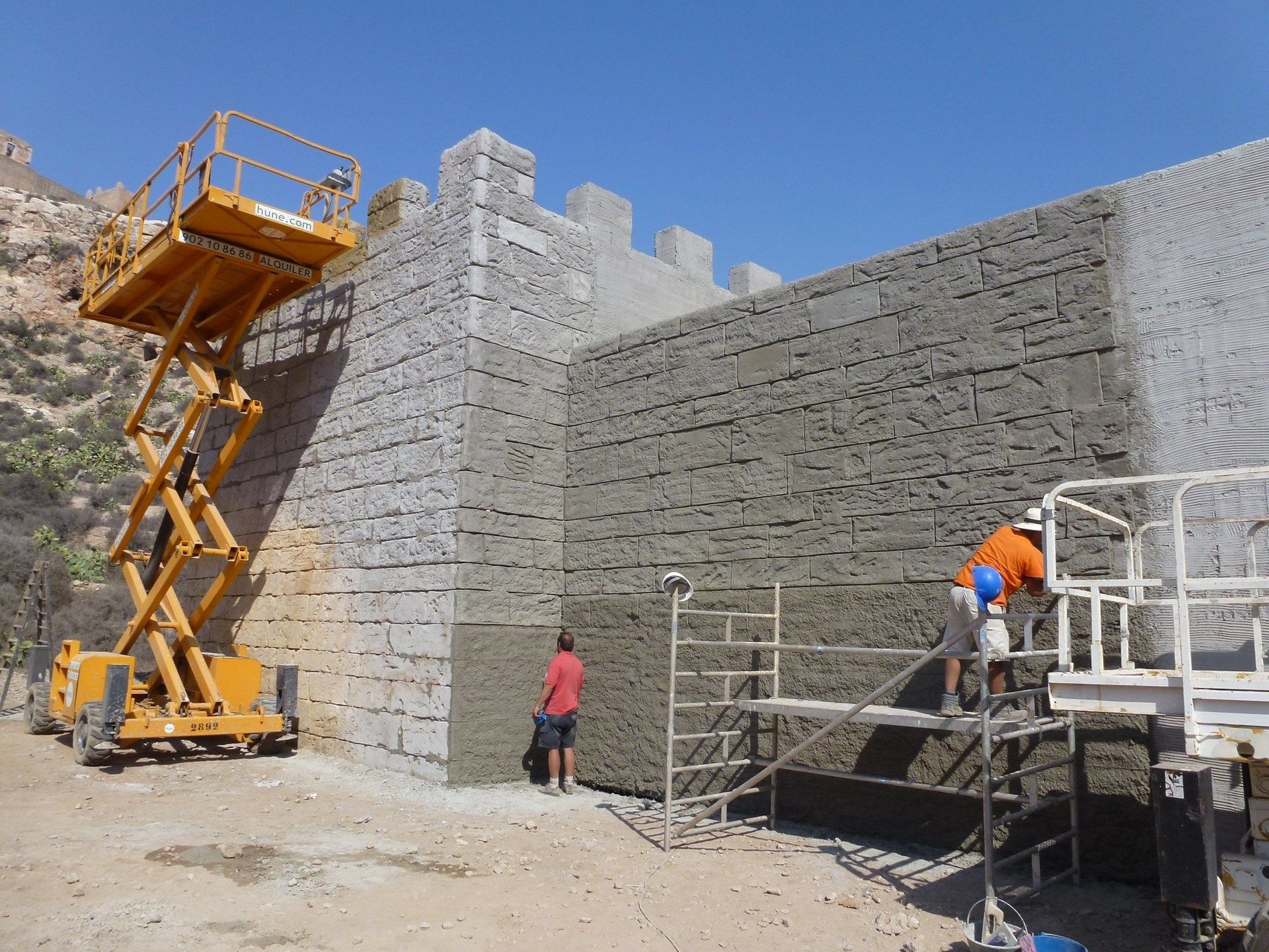 Una obra en construcción con un elevador de tijera amarillo al fondo