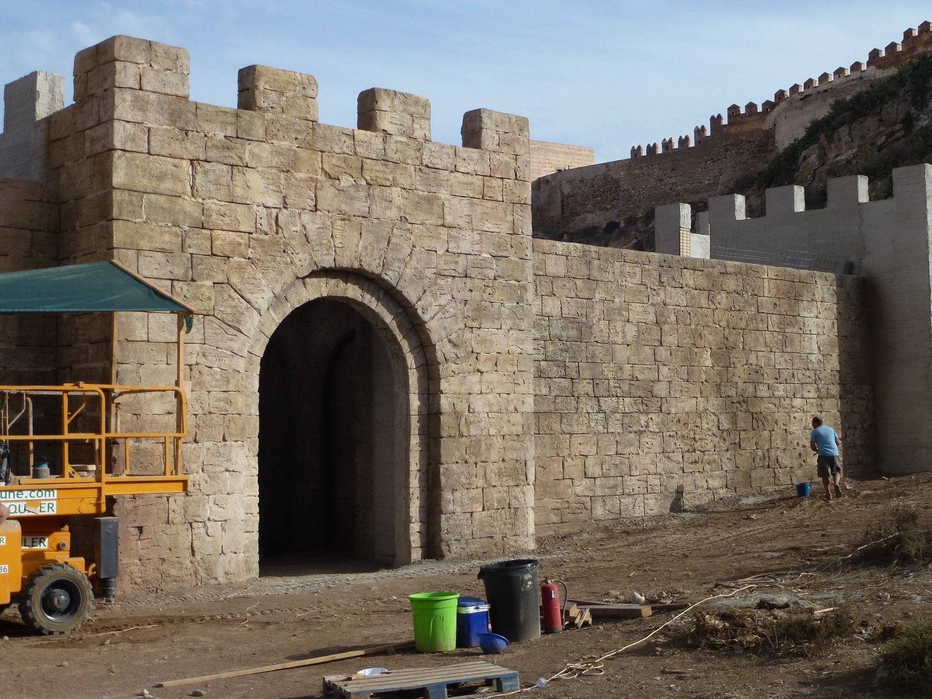 Un tractor amarillo está estacionado frente a un gran muro de piedra.