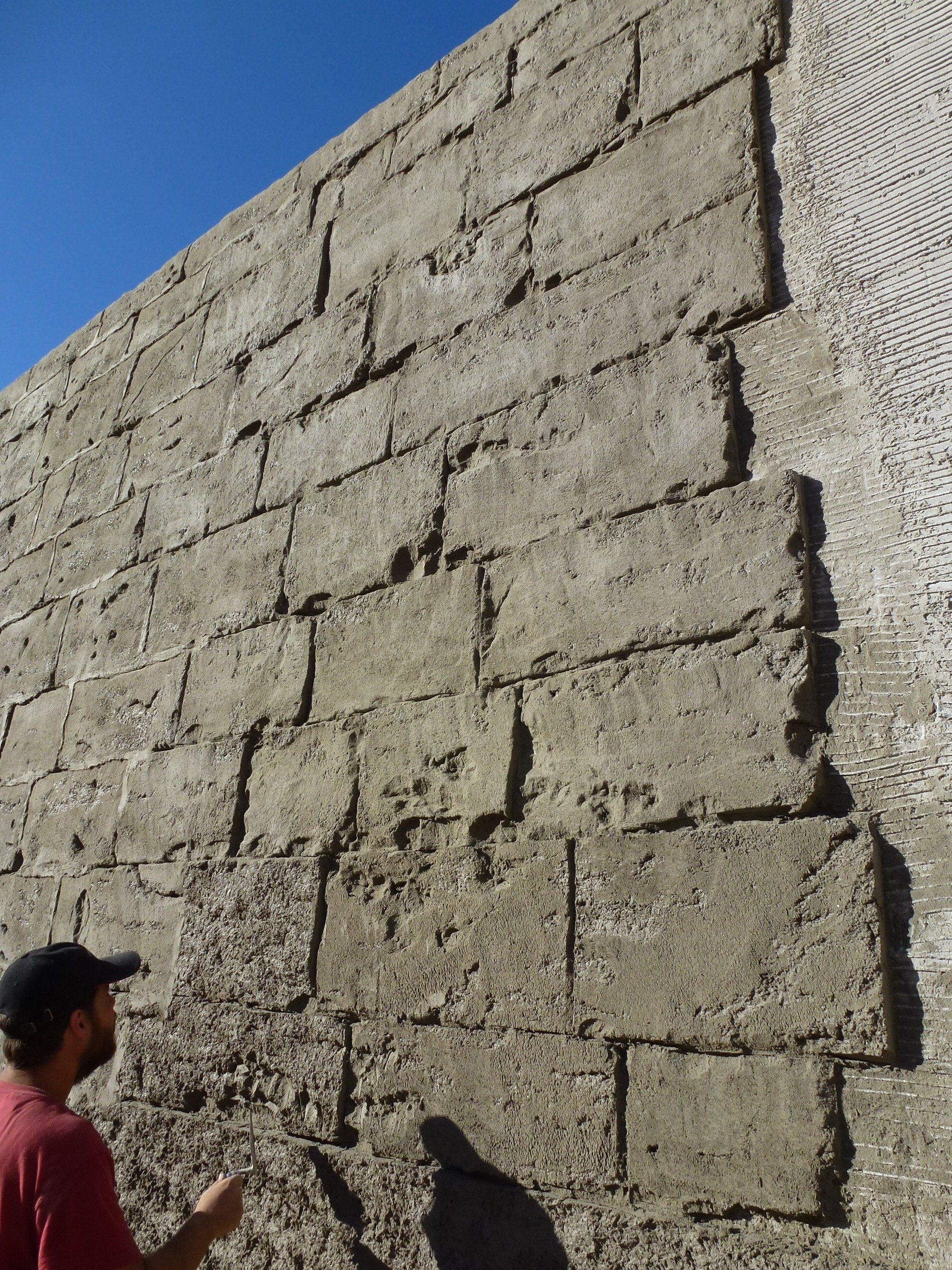 Un hombre parado frente a una gran pared de ladrillos