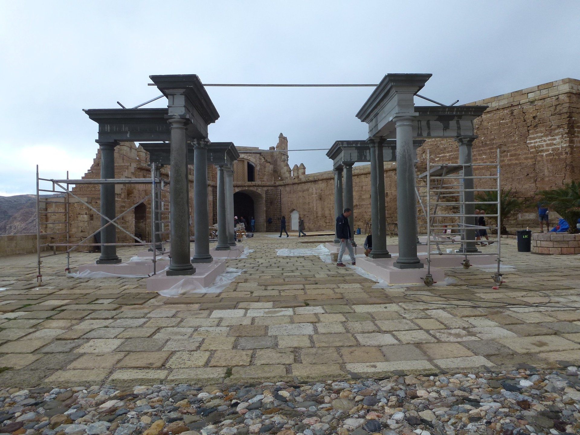 Una pasarela de piedra con columnas y andamios frente a un edificio.