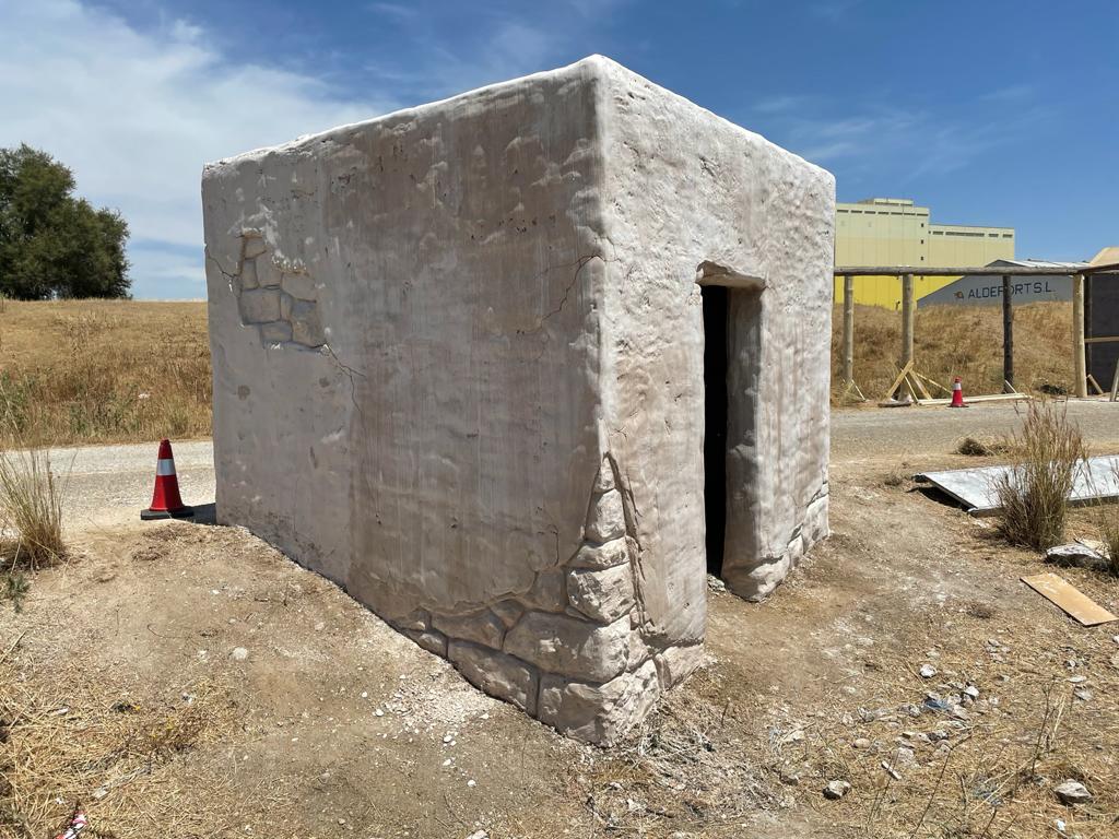 Un pequeño edificio blanco está situado en el medio de un campo de tierra.