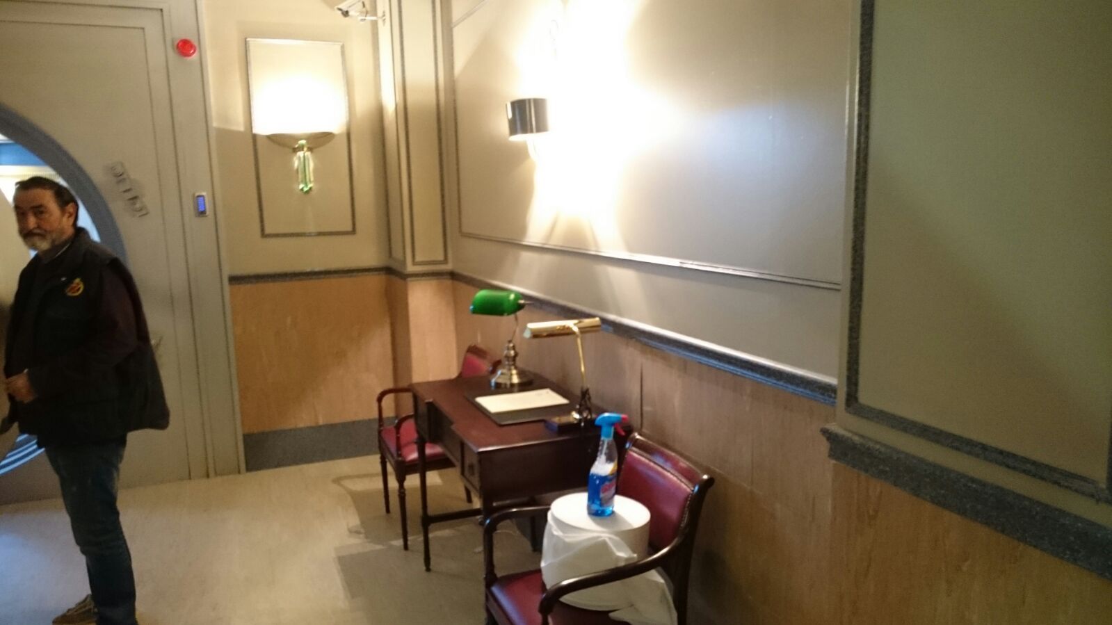 Un hombre está de pie en un pasillo con un escritorio y sillas.
